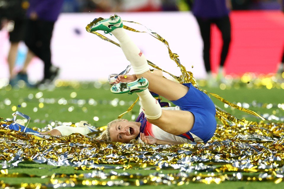 Leah Williamson of England celebrating a victory, lying in ticker tape and confetti.