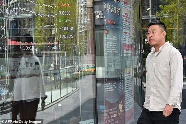 CHINA - A man walks past a screen showing stock prices at a securities office in Beijing today